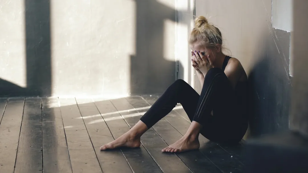 Woman sitting on floor, covering face with hands.