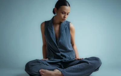 A woman in a vest and pants sits cross-legged.