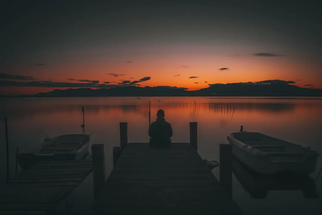 person sitting on dock during sunset