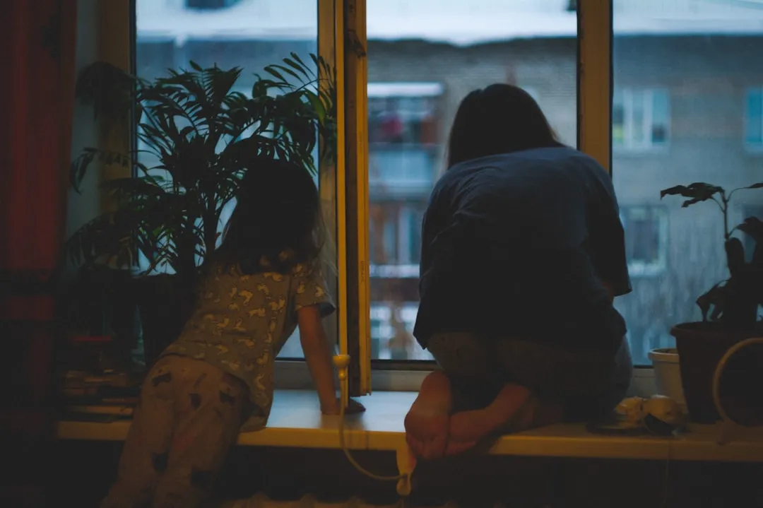 Two people looking out a window at night.