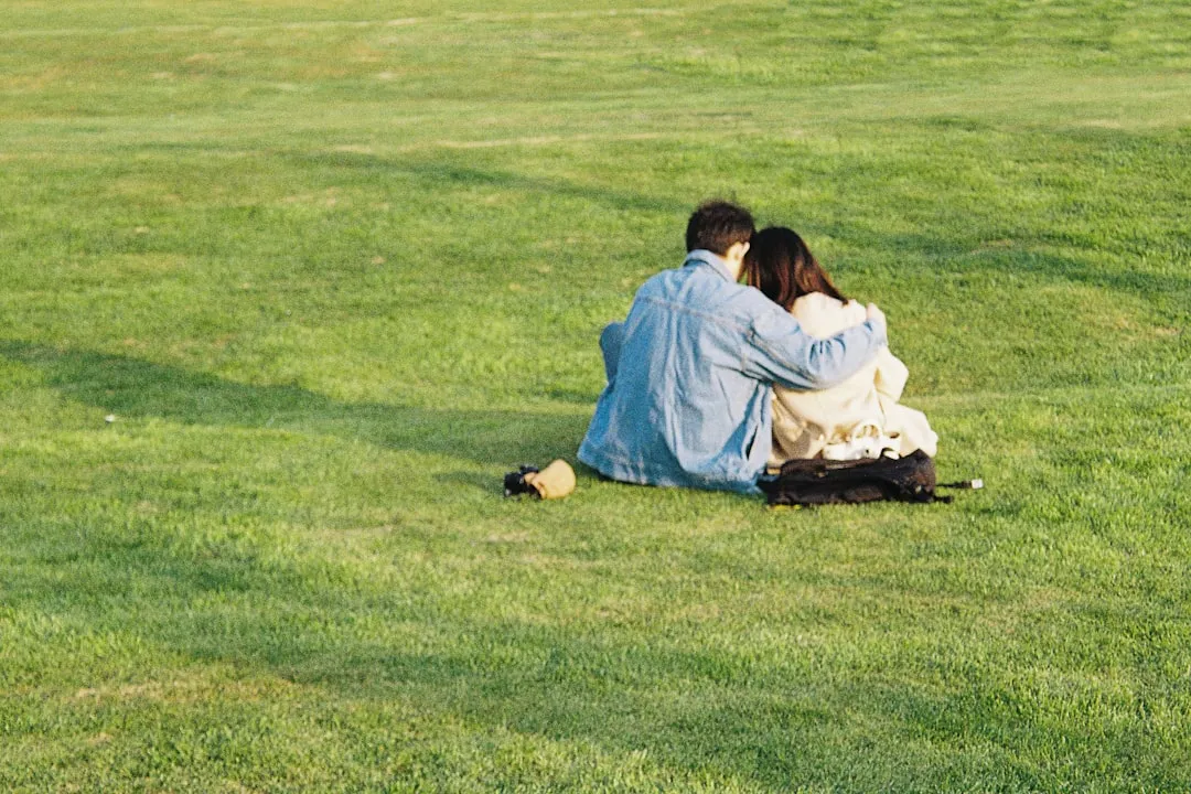 a couple of people sitting on top of a lush green field