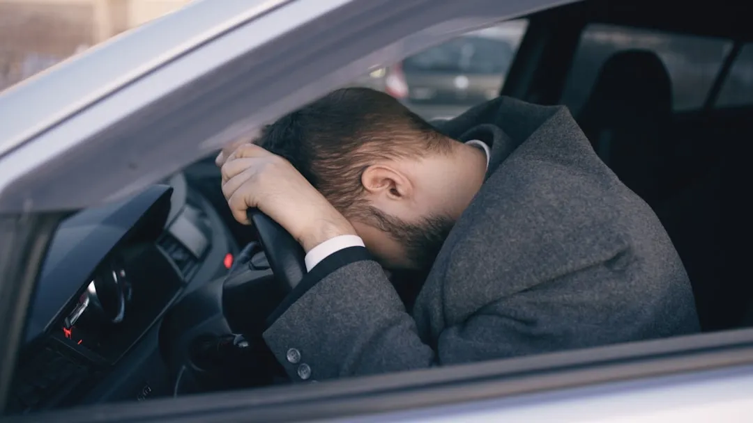 Man resting head on steering wheel inside car.