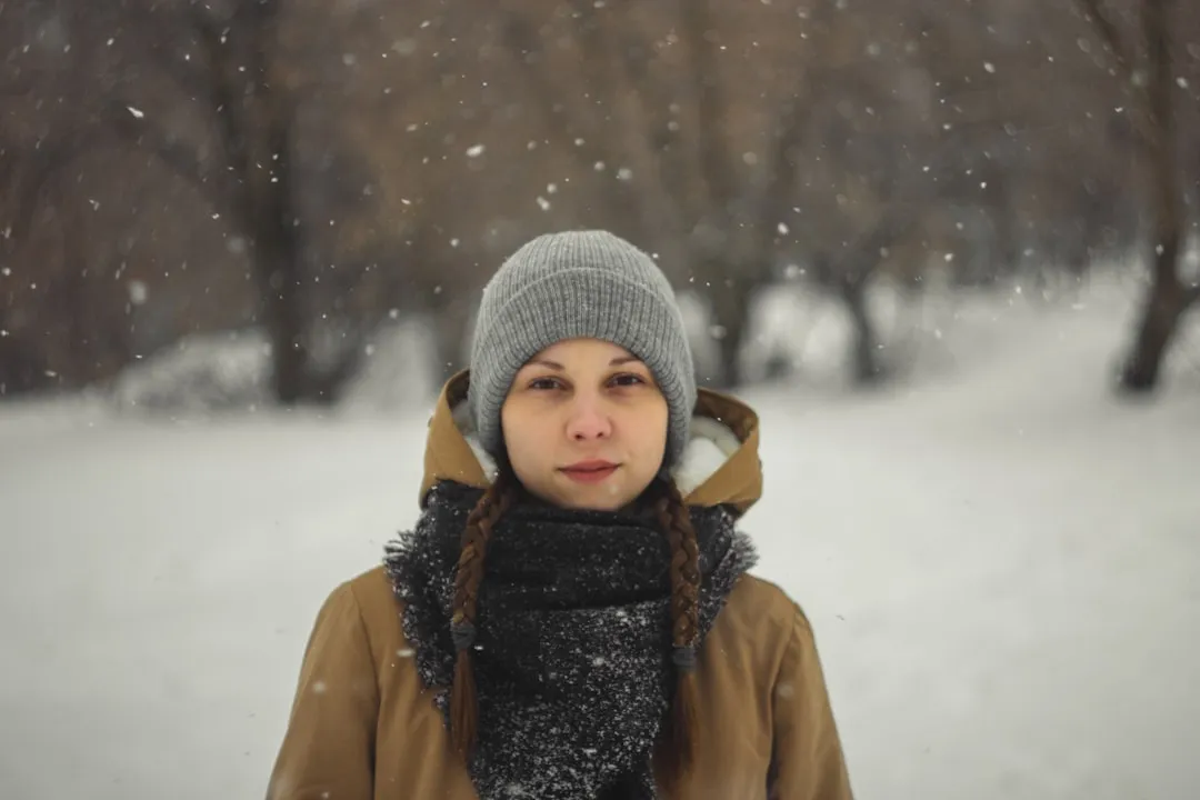 child in gray knit cap and brown coat on snow covered ground during daytime