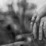grayscale photo of two person holding hands with wedding rings
