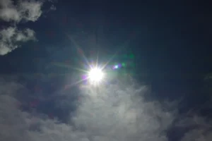 The bright sun shines through cloudy skies.