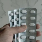 Hand holding blister packs of white pills