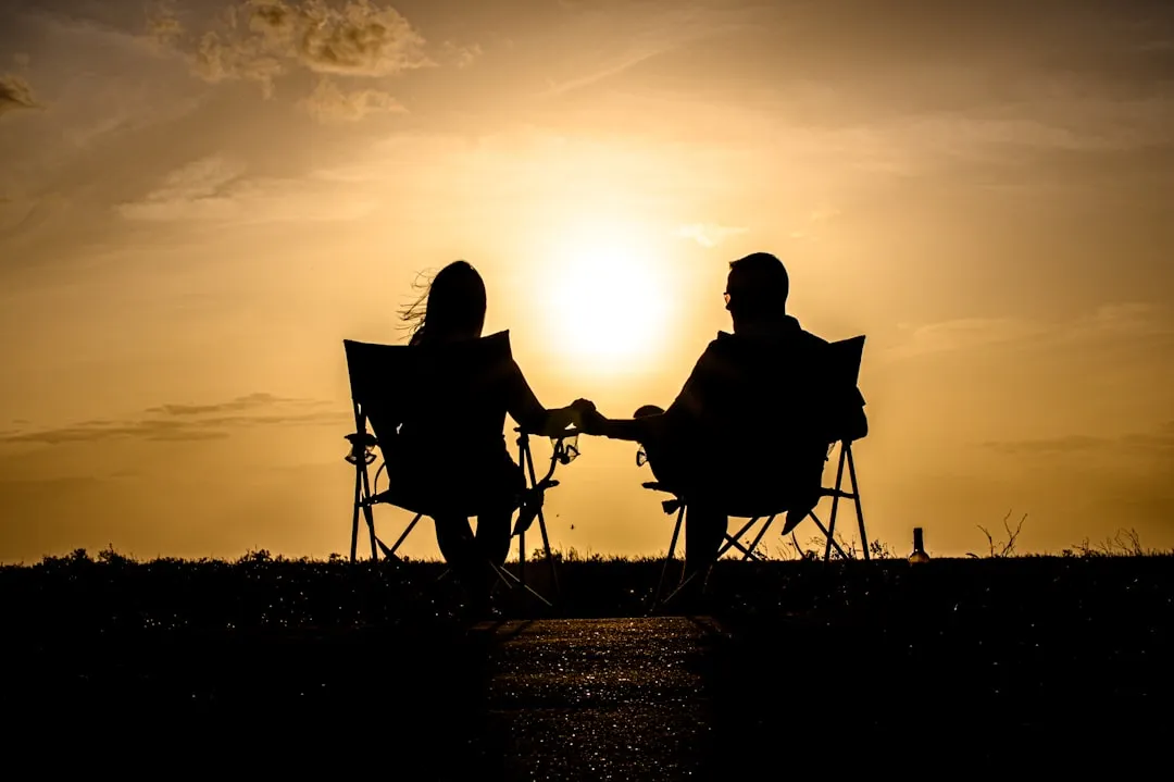 a man and woman sitting on a chair in front of a sunset