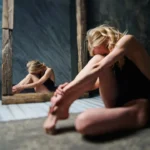 a woman sitting on the floor in front of a mirror