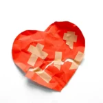 A broken red heart taped together on white background