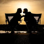 a couple of people sitting on a bench with a sunset in the background