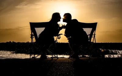 a couple of people sitting on a bench with a sunset in the background