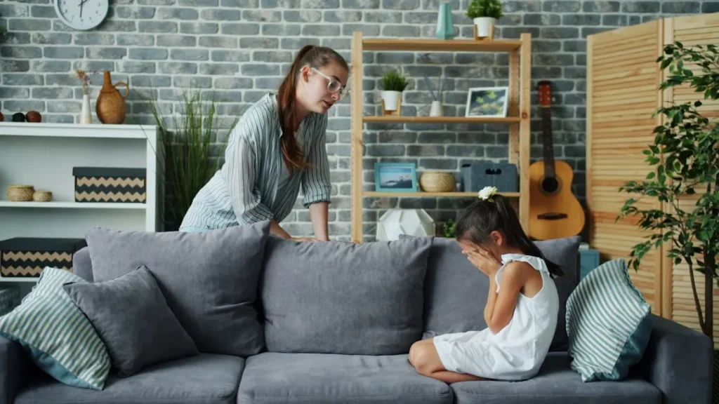 Mother scolds crying daughter on sofa in living room.