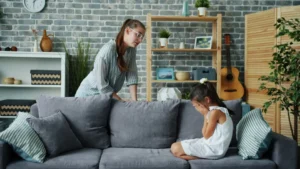 Mother scolds crying daughter on sofa in living room.