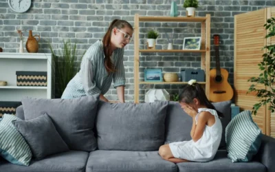 Mother scolds crying daughter on sofa in living room.