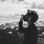 man drinking water on top of mountian