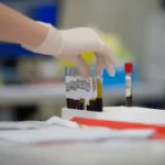 a gloved hand holding a test tube filled with blood