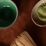 Matcha powder in a wooden spoon with whisk and bowl
