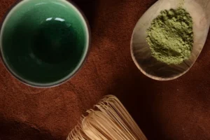 Matcha powder in a wooden spoon with whisk and bowl