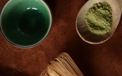Matcha powder in a wooden spoon with whisk and bowl