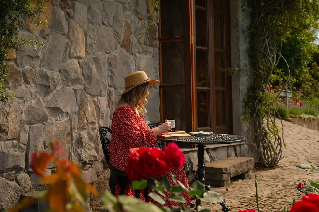 Woman in hat drinks coffee at outdoor table.