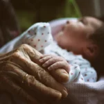 a baby sleeping in a blanket next to an older woman