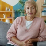 Elderly woman sitting on a couch in a living room.