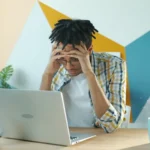Man holding head in frustration at desk with laptop.