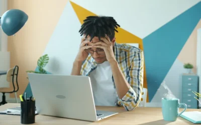 Man holding head in frustration at desk with laptop.