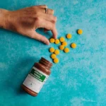 a hand reaching for a bottle of pills on a blue surface