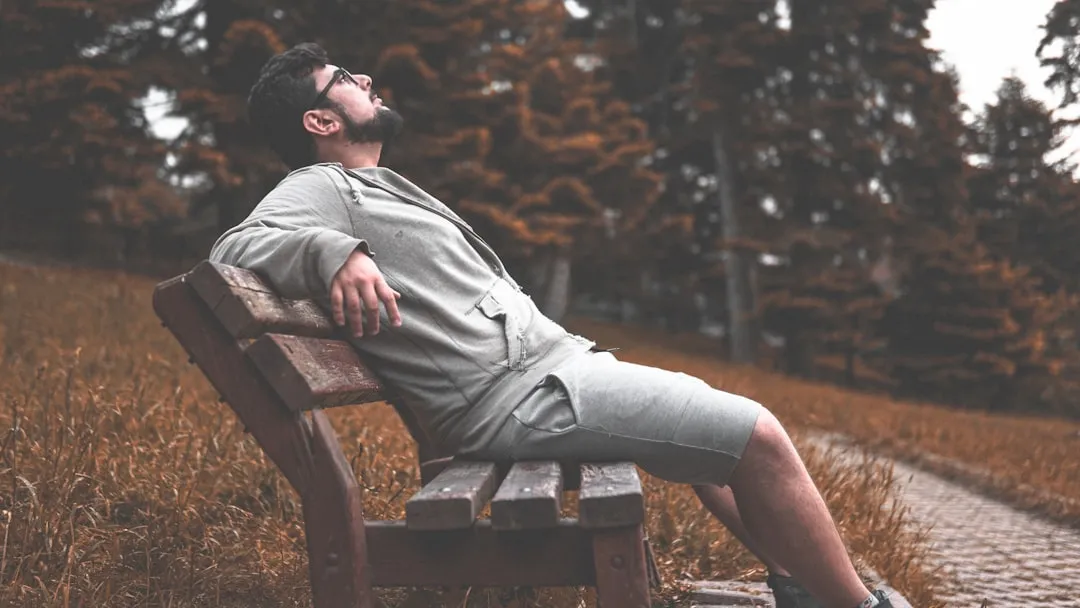 man wearing gray jacket sitting in wooden bench while looking up