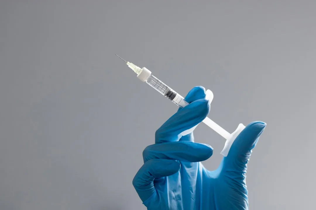 A hand in a glove holds a syringe.