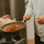 A woman cooking food in a frying pan on a stove