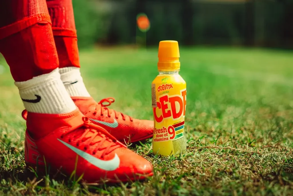 Red soccer cleats and a drink on grass.