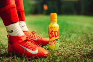 Red soccer cleats and a drink on grass.