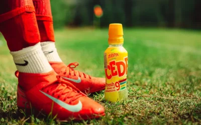 Red soccer cleats and a drink on grass.